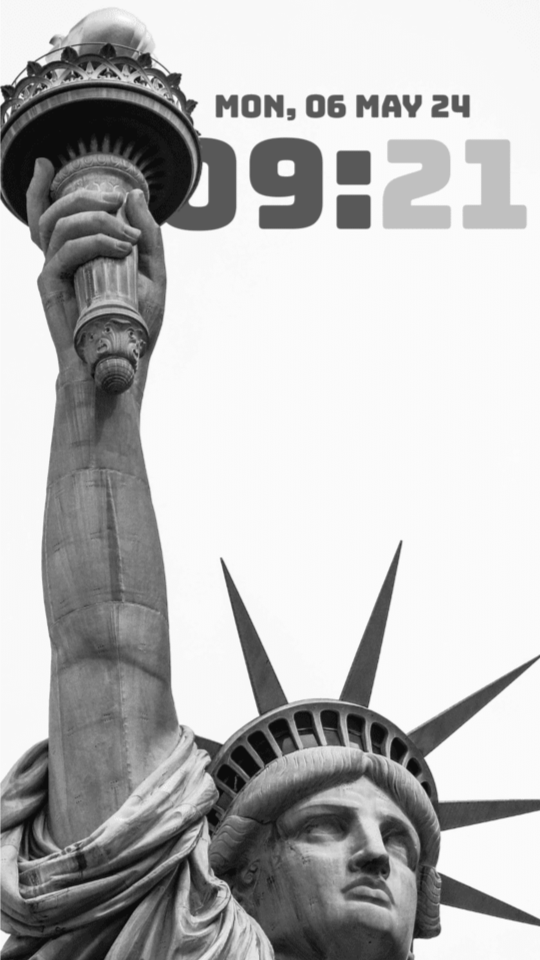 Black and white Statue of Liberty torch and head against a white sky, with a bold grey 09:21 clock partly hidden behind the raised arm.